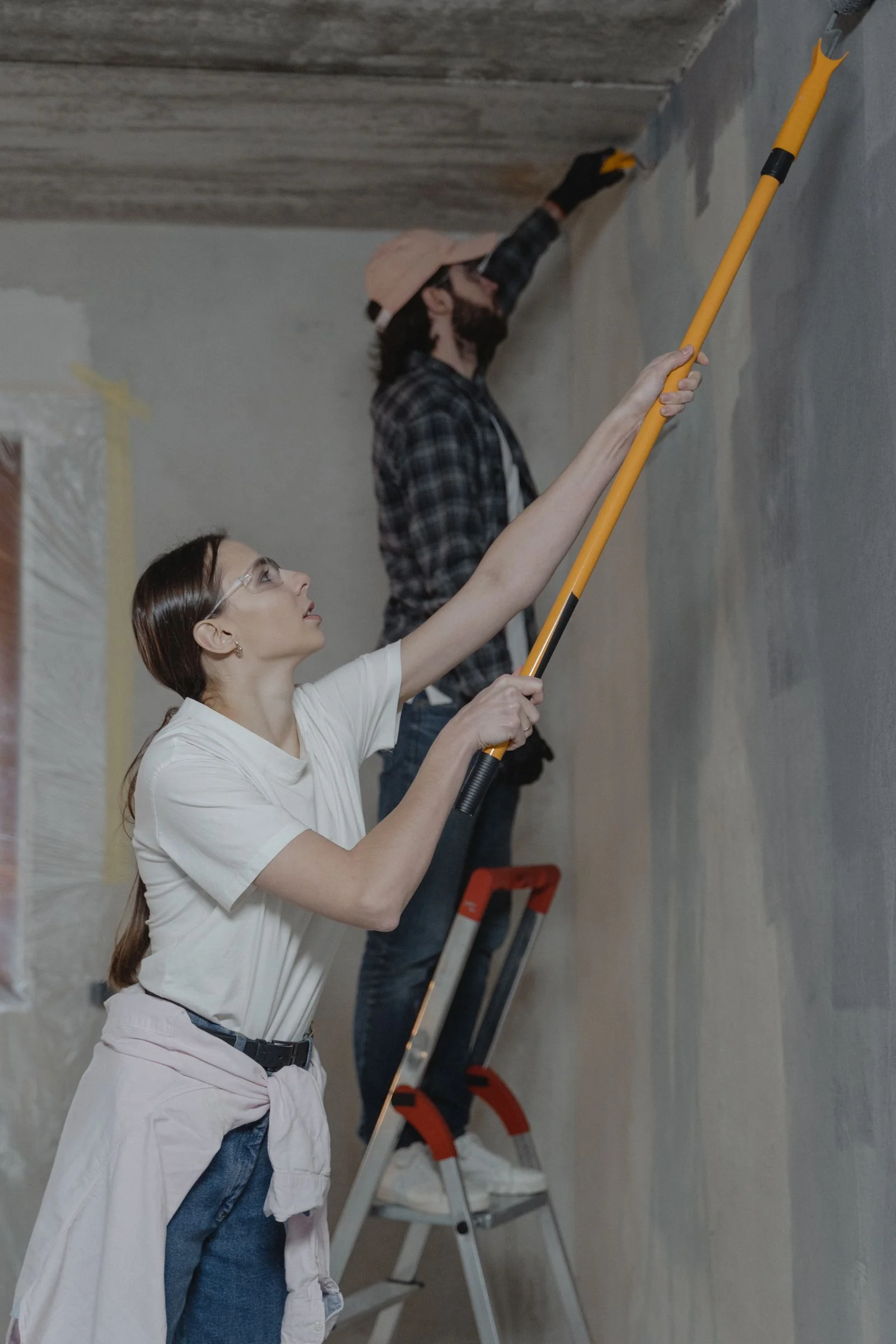 Two people painting a home interior with rollers